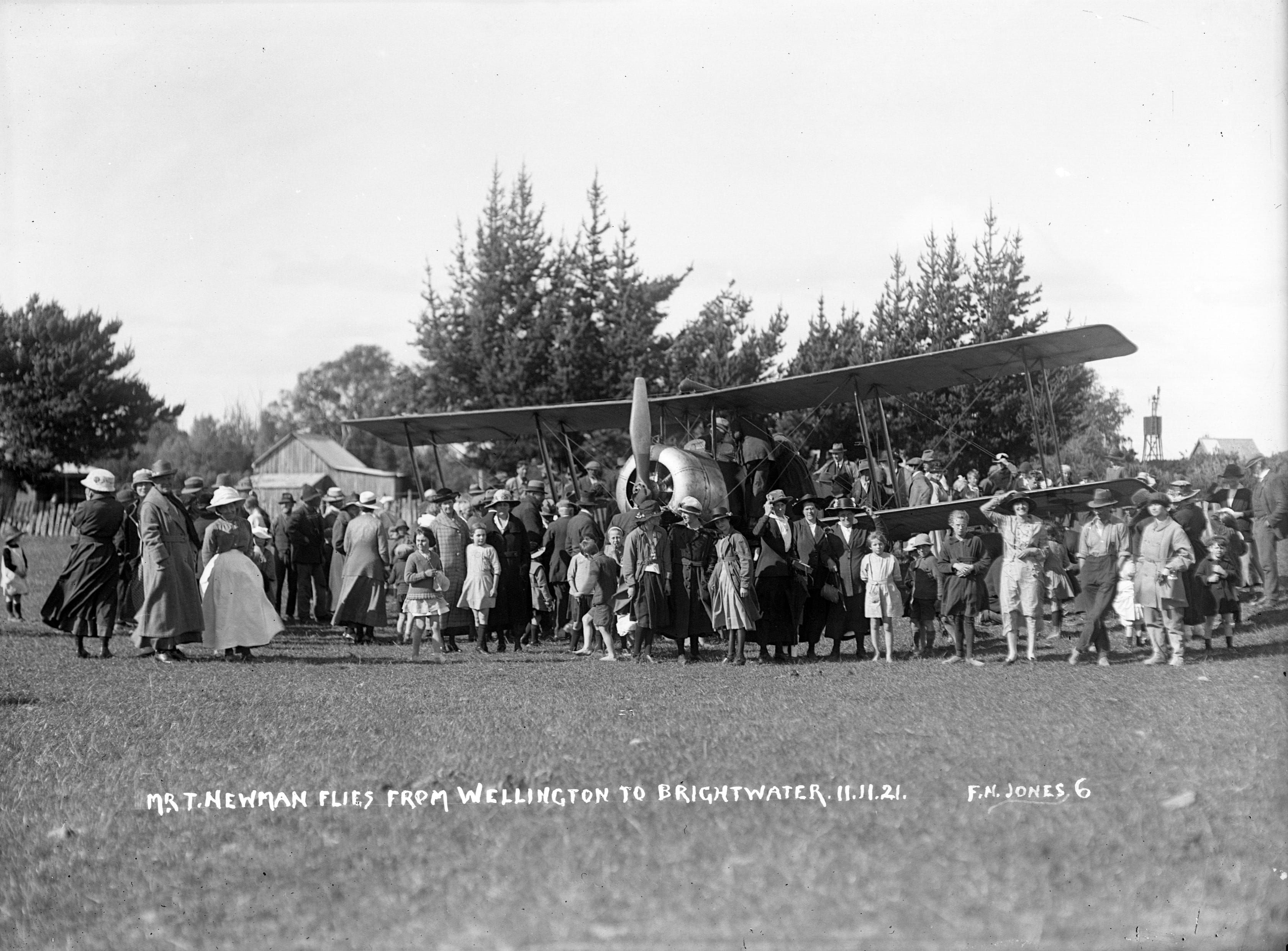 Black and white photo a biplane parked in a field surrounded by a crowd.